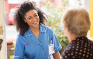 Elderly woman opens the door to her smiling professional caregiver