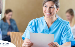 A woman in scrubs holds a paper while interviewing with someone else, representing how a solid caregiver resume can get you to an interview.