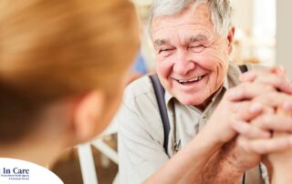 A caregiver holds hands with a happy older client, representing the results of creating a comfortable environment in the home.