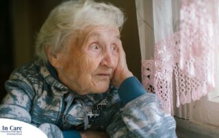 An older woman peacefully looks out of the window while the sun is still up, representing what can happen with sundowning.