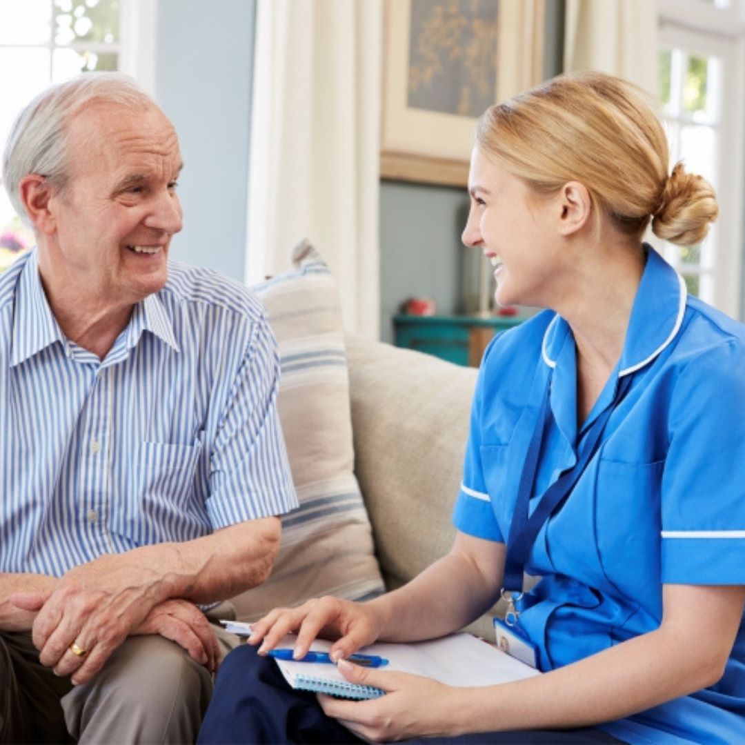 A cheerful care giver sits with and elderly patient laughing.