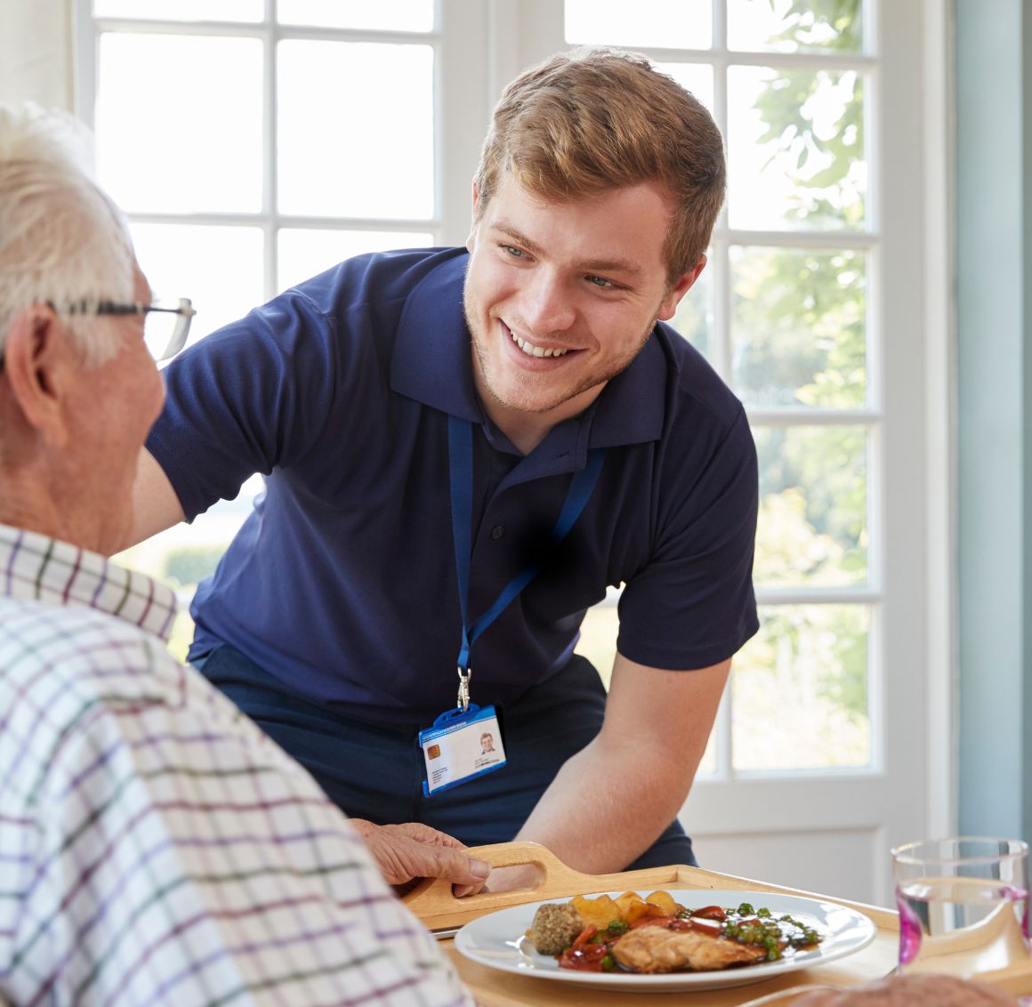 Personal Care in Bradenton. An elderly man sits at a table as a cheerful care giver hands him a plate of food.